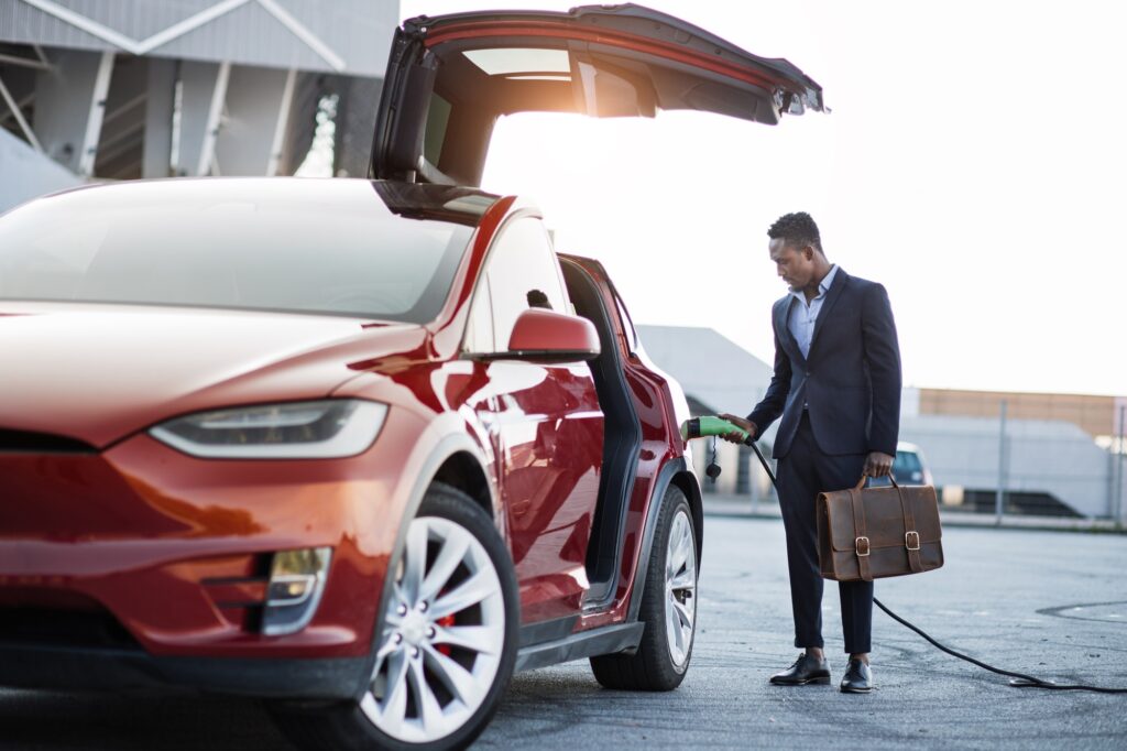 African businessman with suitcase charging electric car